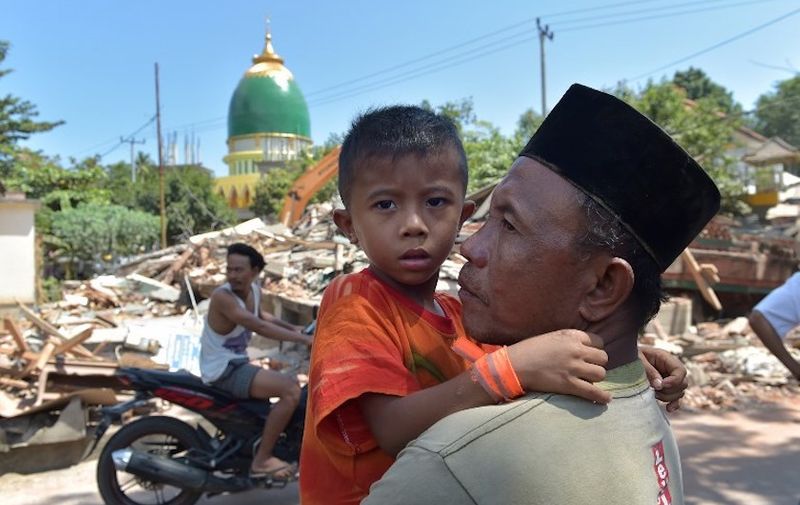 An Indonesian man holds a boy across from collapsed buildings as search and rescue members search for a victim of the recent quake in Tanjung on Lombok island on August 9, 2018.
A strong aftershock struck Indonesia's Lombok on August 9, causing panic among evacuees sheltering after a devastating earthquake killed more than 160 on the holiday island four days earlier. / AFP PHOTO / ADEK BERRY