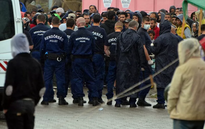 Hungarian pilice officers stand on guard in the refugee camp of the Hungarian-Serbian border Roszke village on August 26, 2015 as tear gas have been deployed by police when about 200 migrants refused to give fingerprints and tried to leave the camp. More than 140,000 migrants have reached Hungary on routes across the Balkans so far in 2015. Recently, some 80 percent of them are from war zones like Syria, Iraq and Afghanistan.   AFP PHOTO / CSABA SEGESVARI
