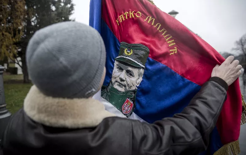 In this photograph taken on December 9, 2017, a Serbian nationalist holds a flag with an image of Bosnian Serb convicted war criminal Ratko Mladic, as he prepares to enter St. Sava Church in Belgrade, to attend prayers for the former Bosnian Serbian commander. Ratko Mladic, the wartime Bosnian Serb military chief, was given a life sentence on November 22, by the International Criminal Tribunal for the former Yugoslavia (ICTY) in The Hague, for genocide during the country's inter-ethnic war in the 1990s. (Photo by OLIVER BUNIC / AFP)