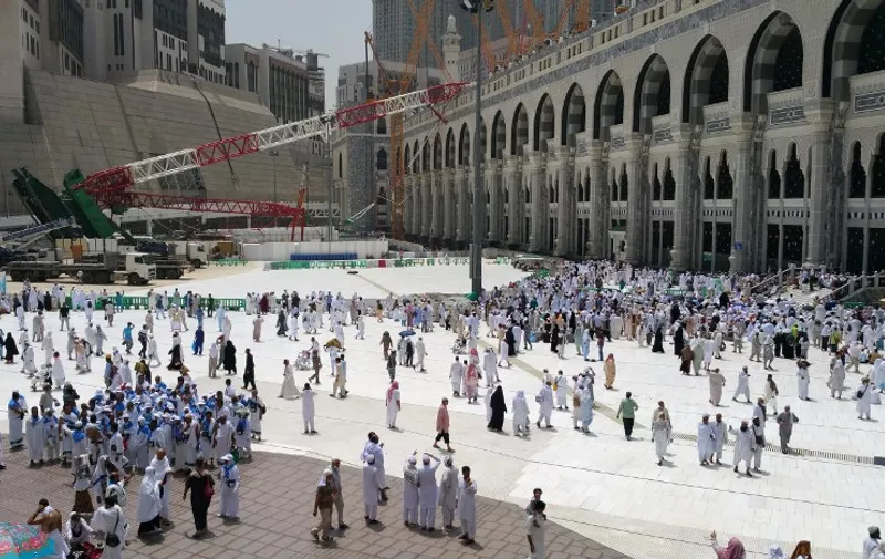 Muslim pilgrims walk past the crane that collapsed the day before at the Grand Mosque in Saudi Arabia's holy Muslim city of Mecca on September 12, 2015. This year's hajj pilgrimage will go ahead despite a crane collapse which killed more than 100 people at the Grand Mosque of Mecca, a Saudi official told AFP.     AFP PHOTO / STR