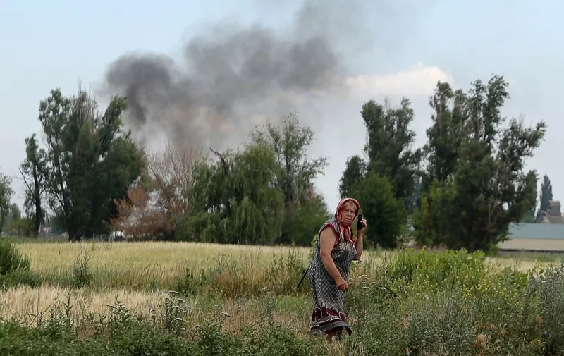 A woman speaks on a mobile phone on a roadside while smoke rises behind in the village Sviato-Pokrovske, Donetsk region, on June 23, 2022, amid Russia's military invasion launched on Ukraine. - On the road between the towns of Siversk and Bakhmut, AFP journalist witnessed several shellings on the route, which is now the main itinerary being used to reach the city of Lysychansk, since a highway has long been under shelling. Driving out of the devastated eastern Ukrainian city of Lysychansk on June 23, the journalists twice had to jump out of cars and lie on the ground as Russian forces shelled the city's main supply road. The three shelling incidents they witnessed took place on a stretch of road approximately 5 kilometres (3 miles) long. (Photo by Anatolii Stepanov / AFP)