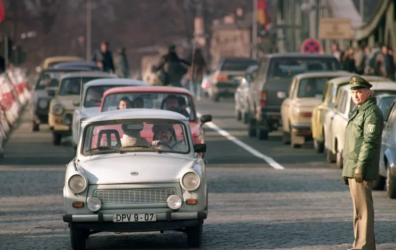 An East German policeman (Vopo) looks at East German Trabant cars, as heavy East to West traffic clogged the Glienicker Bridge, the bridge where East West spy exchanges traditionnally took place, on November 21, 1989. On November 09, Gunter Schabowski, the East Berlin Communist party boss, declared that starting from midnight, East Germans would be free to leave the country, without permission, at any point along the border, including the crossing-points through the Wall in Berlin. The Berlin concrete wall was built by the East German government 13 August 1961 to seal off East Berlin from the part of the city occupied by the three main Western powers to prevent mass illegal immigration to the West. According to the "August 13 Association" which specialises in the history of the Berlin Wall, at least 938 people - 255 in Berlin alone - died, shot by East German border guards, attempting to flee to West Berlin or West Germany. The wall was opened 09 November 1989 and has been demolished since then. (Photo by GERARD MALIE / AFP)