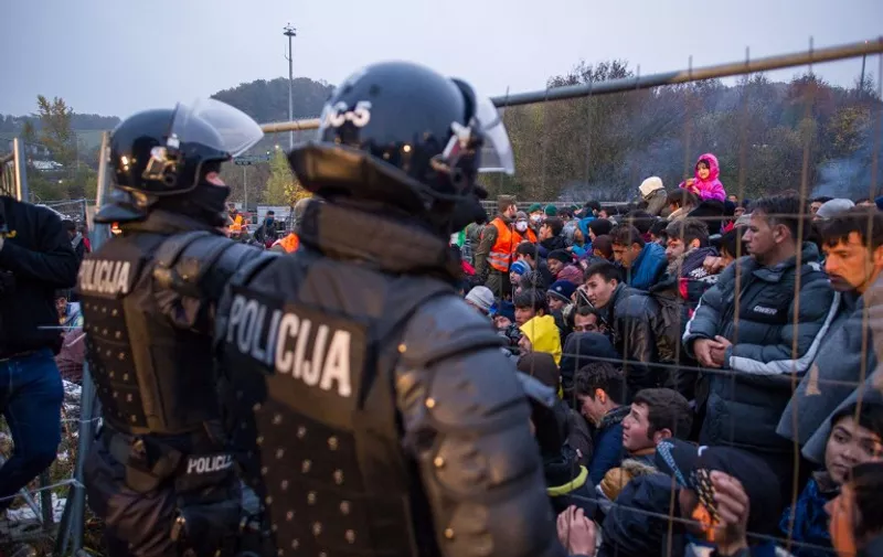 Slovenian riot policemen stand by a fence as a crowd of migrants and refugees wait to cross the Slovenian-Austrian border in Sentilj, Slovenia, to Spielfeld, Austria, on October 29, 2015. Austria on October 28  announced plans to build a fence at a major border crossing with fellow EU state Slovenia to "control" the migrant influx, in a blow to the bloc's cherished passport-free Schengen zone. AFP PHOTO / RENE GOMOLJ