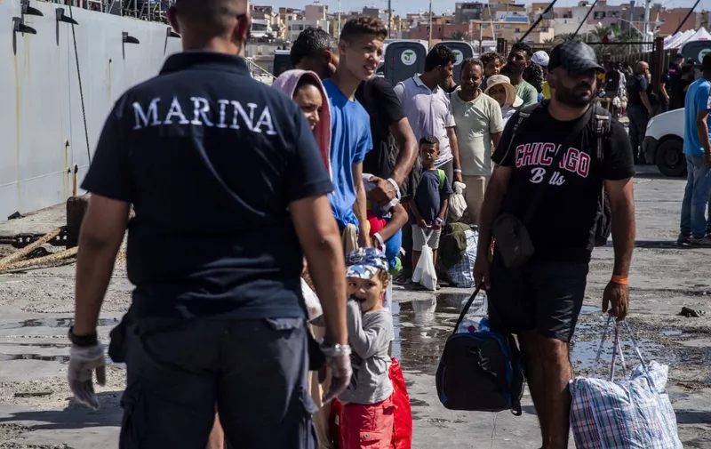 Migrants gather in the harbour of Italian island of Lampedusa, before being transferred to Porto Empedocle in Sicily region, south Italy, by the Italian military ship Cassiopea, on September 15, 2023. The island's reception centre, built to house fewer than 400 people, was overwhelmed with men, women and children forced to sleep outside on makeshift plastic cots, many wrapped in metallic emergency blankets. Good weather has seen a surge in arrivals across Italy in recent days, with more than 5,000 people landing across the country on September 12, and almost 3000 the day after, according to updated interior ministry figures. (Photo by Alessandro SERRANO / AFP)
