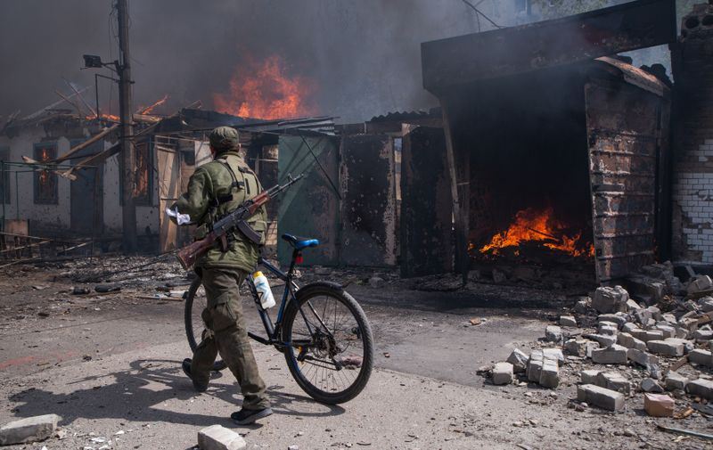 LUGANSK REGION, UKRAINE - MAY 10, 2022: A serviceman of the Lugansk People's Republic militia pushes a bicycle past burning structures in a market in the town of Popasnaya which came under control of the Lugansk People's Republic on 8 May. The Russian Armed Forces are carrying out a special military operation in Ukraine in response to requests from the leaders of the Donetsk People's Republic and Lugansk People's Republic for assistance. Alexander Reka/TASS,Image: 690096484, License: Rights-managed, Restrictions: , Model Release: no, Credit line: Profimedia