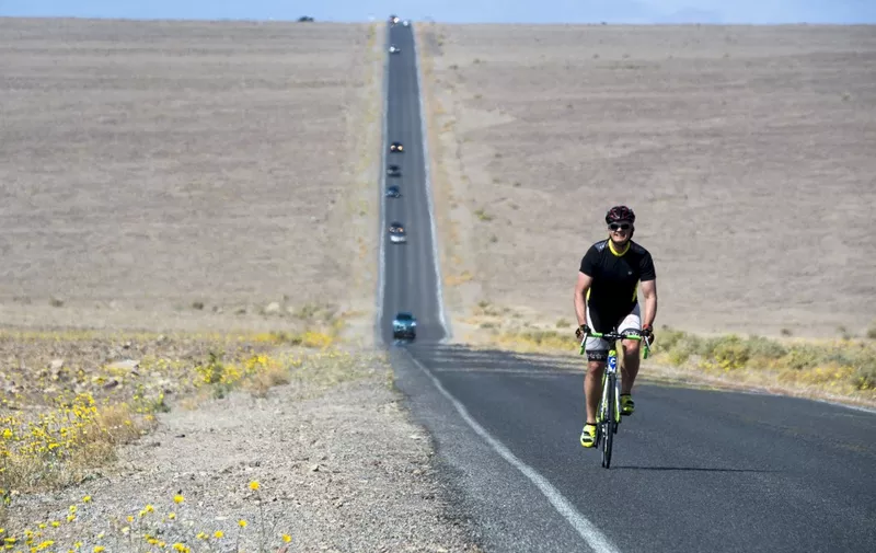 A bicyclists rides along a wildflower-lined highway through Death Valley National Park, in Death Valley, California, March 4, 2016. - Unusally heavy rainfall in October trigged a "super bloom," carpeting Death Valley National Park, the hottest and driest place in North America, in gold, purple, white and pink. The bloom is the parks largest in a decade. (Photo by ROBYN BECK / AFP)