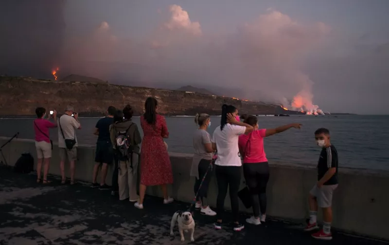 People observe the lava of the Cumbre Vieja volcano falling into the ocean from the port of Tazacorte, in the Canary Island of La Palma on October 6, 2021. - It has been more than two weeks since La Cumbre Vieja began erupting, forcing more than 6,000 people out of their homes as the lava burnt its way across huge swathes of land on the western side of La Palma in Spain's Canary Islands. (Photo by JORGE GUERRERO / AFP)