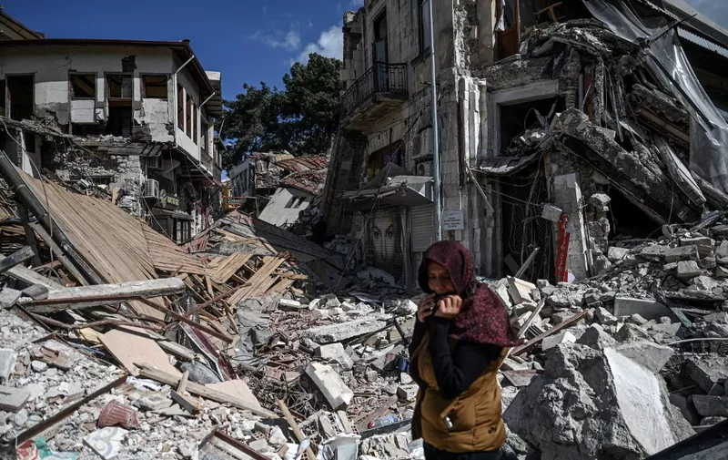 A woman stands among the rubble of collapsed buildings in Hatay on March 6, 2023, one month after a massive earthquake struck southeastern Turkey. - A massive 7.8-magnitude earthquake rocked huge swathes of Turkey and parts of Syria on February 6, 2023, killing more than 50,000 people in both countries, with some 46 000 on the Turkish side. One month on, teams of workers are still toiling to clear the rubble that now dominates quake-hit cities, as the country faces faces the daunting task of rebuilding flattened cities, with tens of thousands buried and many survivors barely subsisting in tents or containers. Turkish officials said 214,000 buildings collapsed following the quake, many of them in Hatay and Kahramanmaras. (Photo by OZAN KOSE / AFP)