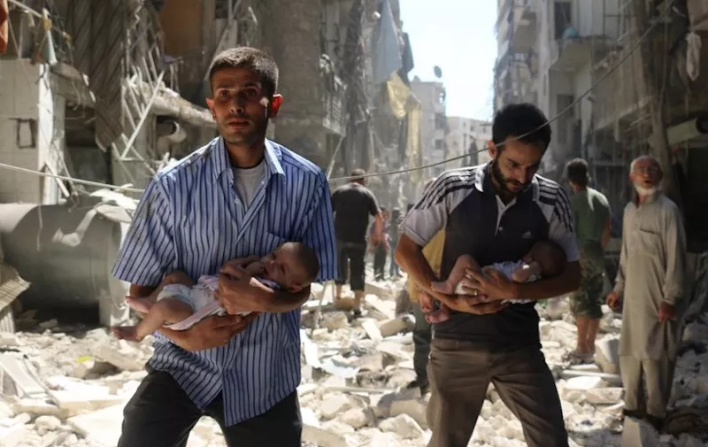 Syrian men carrying babies make their way through the rubble of destroyed buildings following a reported air strike on the rebel-held Salihin neighbourhood of the northern city of Aleppo, on September 11, 2016. - Air strikes have killed dozens in rebel-held parts of Syria as the opposition considers whether to join a US-Russia truce deal due to take effect on September 12. (Photo by AMEER ALHALBI / AFP)
