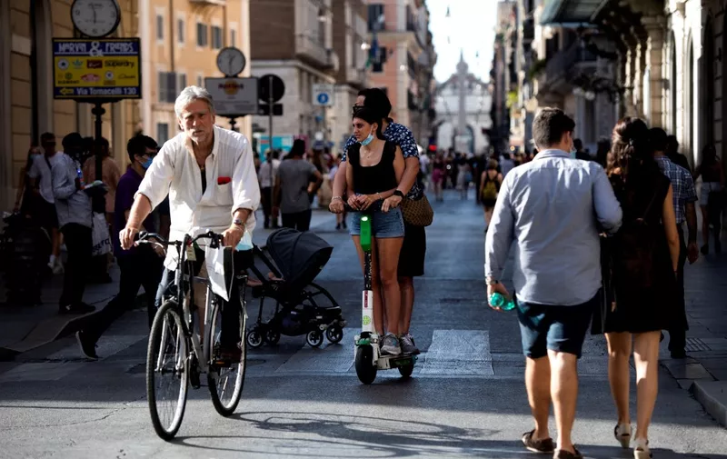 People walk and cycle along a street on the eve of Italy moving into the 'white zone' when it will not be obligatory to wear the mask outdoors in Rome on June 27, 2021. (Photo by Tiziana FABI / AFP)