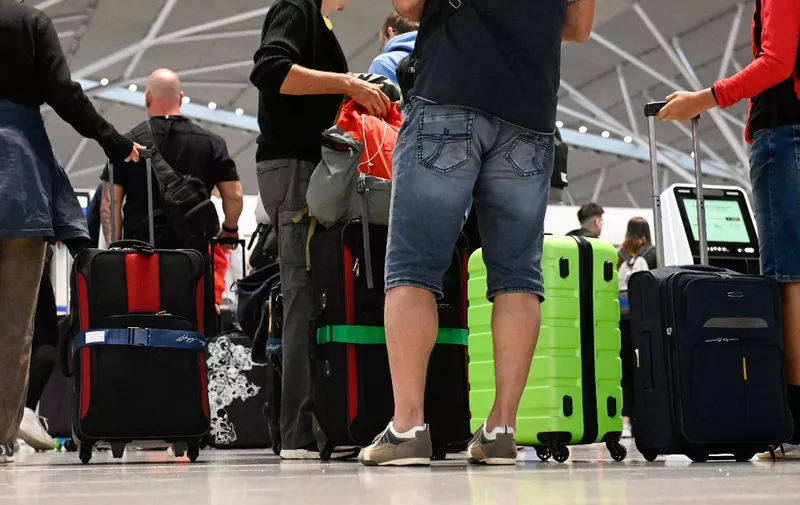 Passengers wearing shorts queue with their luggage in front of a counter for check-in at Stuttgart Airport in Leinfelden-Echterdingen near Stuttgart, southwestern Germany, on July 28, 2023 at the start of the school summer holidays in the federal state of Baden-Wuerttemberg. (Photo by THOMAS KIENZLE / AFP)