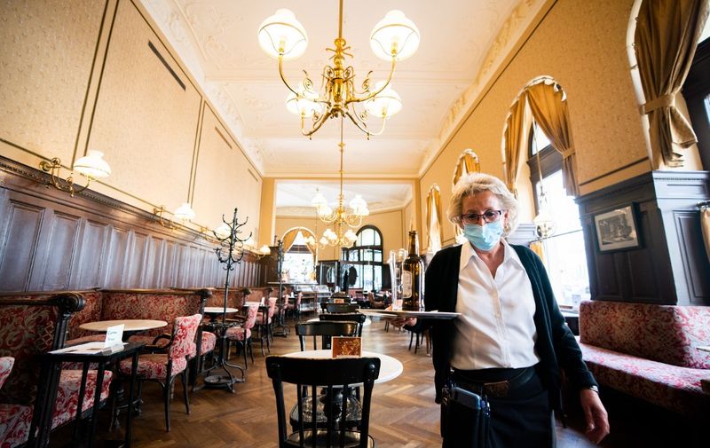 A waitress wearing a face mask carries a tray at Cafe Sperl in Vienna, Austria, on May 16, 2020, after restrictions were eased amid the novel coronavirus / COVID-19 pandemic. (Photo by GEORG HOCHMUTH / APA / AFP) / Austria OUT