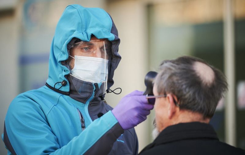 A medical worker measures body temperature at one of the entrances of the Community Health Centre in Kranj, Slovenia on March 23, 2020 amid concerns over the spread of the COVID-19 coronavirus. (Photo by Jure Makovec / AFP)