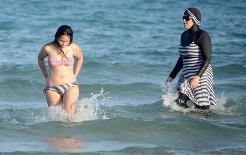 (FILES) This file photo taken on August 16, 2016 shows Tunisian women, one (R) wearing a "burkini", a full-body swimsuit designed for Muslim women, swimming at Ghar El Melh beach near Bizerte, northeast of the capital Tunis. 
The ban on the Islamic burkini swimsuit on some French beaches has triggered disdain in English-speaking countries, where outlawing religion-oriented clothing is seen as hampering integration. / AFP PHOTO / FETHI BELAID