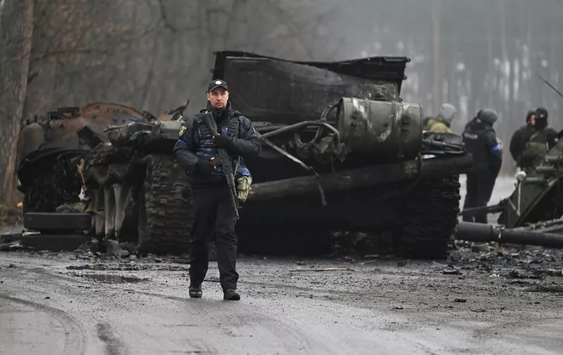 A Ukrainian policeman walks past the wreckage of a Russian armoured vehicle in Dmytrivka village, west of Kyiv, on April 2, 2022 as Ukraine says Russian forces are making a "rapid retreat" from northern areas around Kyiv and the city of Chernigiv. (Photo by Genya SAVILOV / AFP)