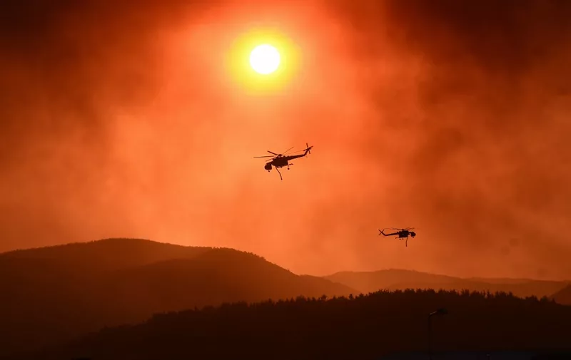 Helicopters fly over as wildfire rages near Alexandroupoli, northern Greece, on August 21, 2023. The European Union announced it was deploying two Cyprus-based fire-fighting aircraft and a Romanian fire-fighting team via the bloc's civil protection mechanism, as wildfires rage uncontrolled in Greece for a third day. (Photo by Sakis MITROLIDIS / AFP)