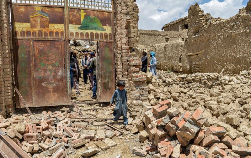 A child walks out from inside a gate of a house damaged by an earthquake in Bernal district, Paktika province, on June 23, 2022. - Desperate rescuers battled against the clock and heavy rain on June 23 to reach cut-off areas in eastern Afghanistan after a powerful earthquake killed at least 1,000 people and left thousands more homeless. (Photo by Ahmad SAHEL ARMAN / AFP)