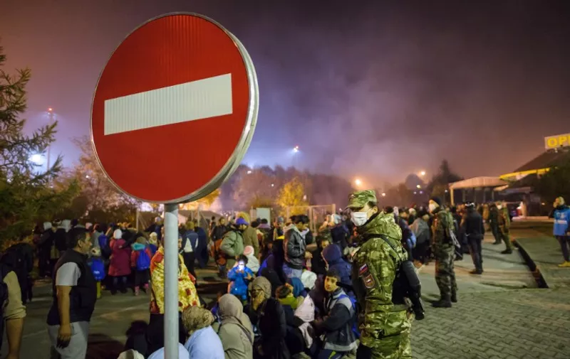 A no entry sign is pictured next to Slovenian servicemen standing guard as migrants and refugees walk towards buses in Sentilj, northeastern Slovenia, on October 28, 2015, to continue their journey and cross the Slovenia-Austria border. European Commission President Jean-Claude Juncker and Austrian Chancellor Werner Faymann warned on October 28 that fences were not welcome in the EU, after Vienna suggested it could build a barrier on its border with Slovenia to control an influx of migrants. Austria and Slovenia have become key transit points for tens of thousands of refugees and migrants seeking to reach northern Europe ahead of the winter. AFP PHOTO / RENE GOMOLJ