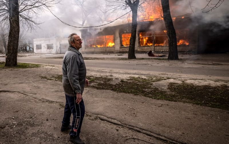 A man stands on a pavement as a house is burning following a shelling Severodonetsk, Donbass region, on April 6, 2022, as Ukraine tells residents in the country's east to evacuate "now" or "risk death" ahead of a feared Russian onslaught on the Donbas region, which Moscow has declared its top prize. - NATO believes Moscow aims to take control of the whole Donbas region in eastern Ukraine with the aim of creating a corridor from Russia to annexed Crimea. (Photo by FADEL SENNA / AFP)