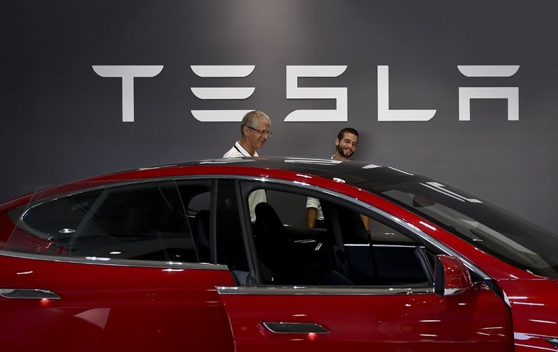 Two man stand in front of a Tesla logo behind the Tesla Model S at the electric carmaker Tesla showroom of El Corte Ingles store in Lisbon, on September 1, 2017. (Photo by PATRICIA DE MELO MOREIRA / AFP)