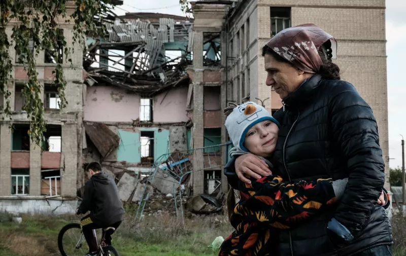 Olga Srednyakova (R), 51, a single mother of the eight children, hugs the youngest daughter Vera, 8, as other ones harvest mushrooms at an abandoned ground of their destroyed school in Konstantinovka in the Donetsk region on October 13, 2022, amid the Russian invasion of Ukraine. (Photo by Yasuyoshi CHIBA / AFP)