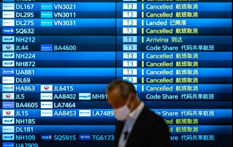 A man walks past an arrivals board showing cancelled flights at Tokyo's Haneda international airport on November 30, 2021, a day after Japan announced it would reinstate tough border measures, barring all new foreign arrivals over the Omicron Covid variant. (Photo by Philip FONG / AFP)