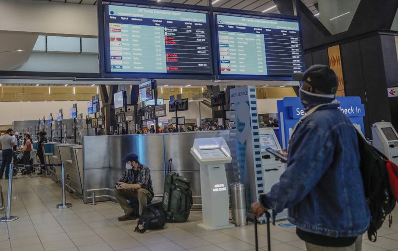 A passenger holds his mobile phone while looking at an electronic flight notice board displaying cancelled flights at OR Tambo International Airport in Johannesburg on November 27, 2021, after several countries banned flights from South Africa following the discovery of a new Covid-19 variant Omicron. - A flurry of countries around the world have banned ban flights from southern Africa following the discovery of the variant, including the United States, Canada, Australia,Thailand, Brazil and several European countries. The main countries targeted by the shutdown include South Africa, Botswana, eSwatini (Swaziland), Lesotho, Namibia, Zambia, Mozambique, Malawi and Zimbabwe. (Photo by Phill Magakoe / AFP)