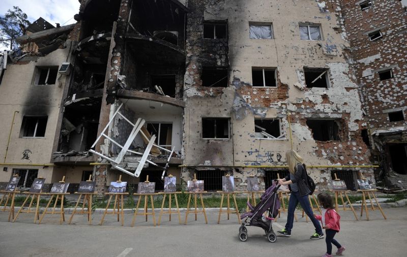 A woman and her daughter walk past a residential building destroyed as a result of shelling in town of Irpin, near  the Ukrainian capital of Kyiv on June 16, 2022, as the Russian-Ukraine war enters its 113th day. (Photo by Sergei CHUZAVKOV / AFP)