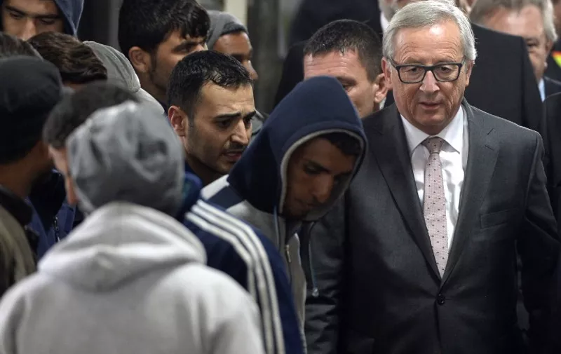 European Commission's President Jean-Claude Juncker (R) walks beside of migrants through a hall during his short visit at the German federal police first refugee's registration point in Passau, southern Germany, on October 8, 2015. AFP PHOTO / CHRISTOF STACHE