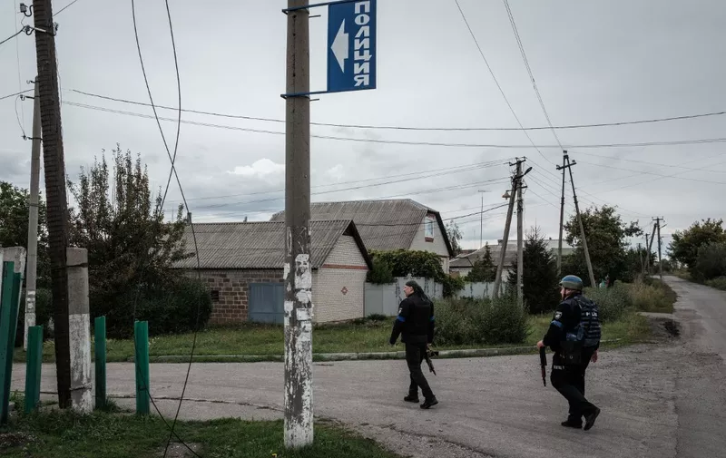 A blue sign reading "police" in Russian spelling is seen as police officers walk towards a police station used during the Russian occupation as a base by a local pro-Russian militia, in the retaken town of Kozacha Lopan, Kharkiv region, on September 20, 2022. - This month's dramatic Ukrainian advance north of Kharkiv drove Russian forces back across the border, and uncovered evidence of torture under their occupation. (Photo by Yasuyoshi CHIBA / AFP)