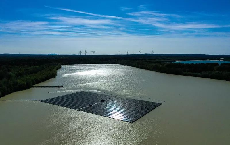 An aerial view shows solar panels at a floating photovoltaic plant on the Silbersee lake in Haltern, western Germany, with wind turbines in the distance on April 22, 2022. - Germany's largest floating solar park is currently being built and will produce almost three million kilowatt hours of electricity per year. (Photo by Ina FASSBENDER / AFP)