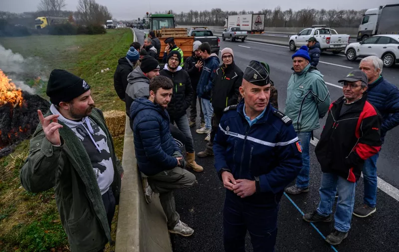Farmers talk with a gendarme as they block a highway to protest over taxation and declining income, near Villefranche-de-Lauragais, outside Toulouse on January 23, 2024. France's powerful farming unions on January 22, 2024 met with French Prime Minister after threatening the government with a week or more of protest action if their demands were not met. The unions have demanded concrete government action to address their grievances, which they say include excessive financial charges and environmental protection rules as well as insufficient prices for their produce. (Photo by Ed JONES / AFP)