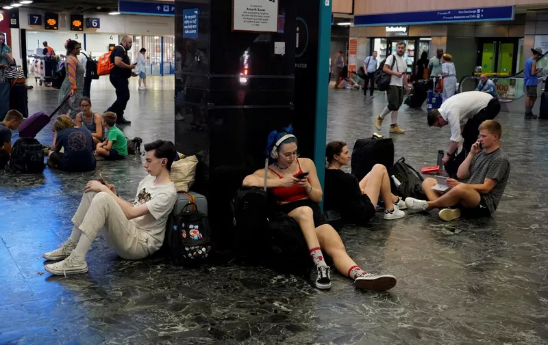 Rail passengers sit with their belongings at Euston train station in central London, on July 19, 2022, as services were cancelled due to a trackside fire, and as the country experiences an extreme heat wave. - All services to and from London Euston were on Tuesday suspended, as emergency services dealt with a fire on the trackside. After the UK's warmest night on record, the Met Office said 40.2C had been provisionally recorded by lunchtime at Heathrow Airport, in west London, taking the country into uncharted territory. (Photo by Niklas HALLE'N / AFP)