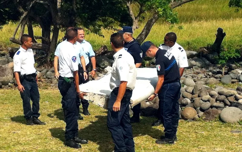 Police and gendarmes carry a piece of debris from an unidentified aircraft found in the coastal area of Saint-Andre de la Reunion, in the east of the French Indian Ocean island of La Reunion, on July 29, 2015.  The two-metre-long debris, which appears to be a piece of a wing, was found by employees of an association cleaning the area and handed over to the air transport brigade of the French gendarmerie (BGTA), who have opened an investigation. An air safety expert did not exclude it could be a part of the Malaysia Airlines flight MH370, which went missing in the Indian Ocean on March 8, 2014. AFP PHOTO / YANNICK PITOU