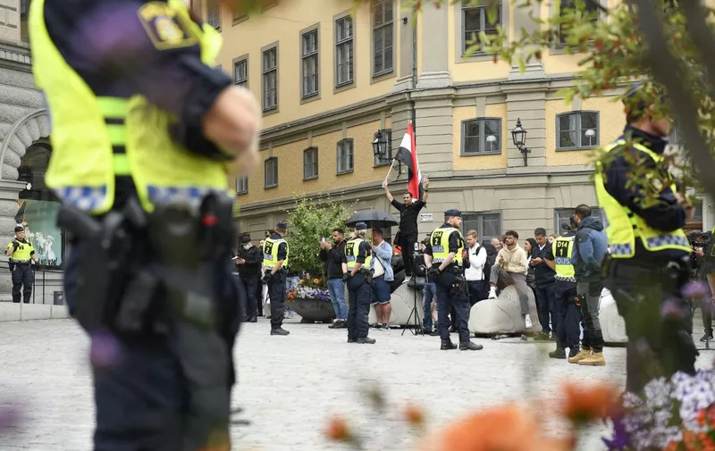 Policemen stand next to demonstrators, among them a protester (background, C) holding the flag of Iraq, at Mynttorget square in Stockholm, Sweden, on July 31, 2023. Two men set the Koran alight outside parliament in Stockholm, an AFP reporter saw, at a protest similar to previous ones that have sparked tensions between Sweden and Middle Eastern countries. (Photo by Oscar OLSSON / TT News Agency / AFP) / Sweden OUT