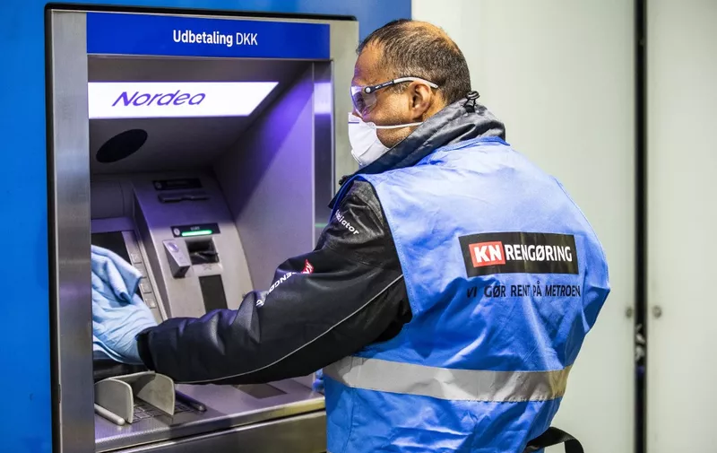 A worker cleans and disinfects a cash dispenser at a metro station in order to better prevent a possible infection with the COVID-19 coronavirus, in Copenhagen, Denmark, on March 31, 2020. (Photo by Olafur Steinar Gestsson / Ritzau Scanpix / AFP) / Denmark OUT