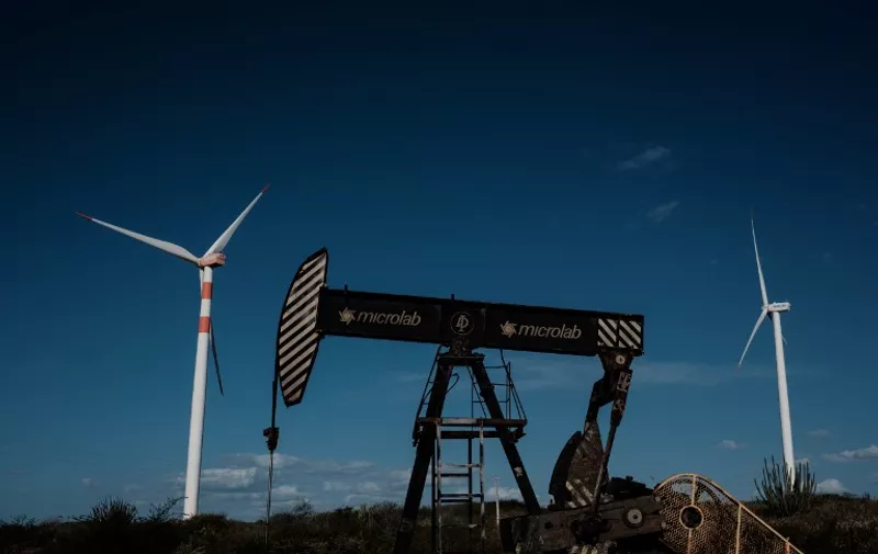 An oil drilling platform is seen next to wind turbines at Vamcruz Windfarm, developed by three energy companies including French renewable energy power plants operator Voltalia Group, on June 29, 2016, in Serra do Mel, Rio Grande do Norte State, Brazil.
Vamcruz Windfarm Complex was inaugurated with 31 wind turbines, which have the potential to supply 200,000 families with energy. / AFP PHOTO / YASUYOSHI CHIBA / TO GO WITH AFP STORY BY MADELEINE PRADEL