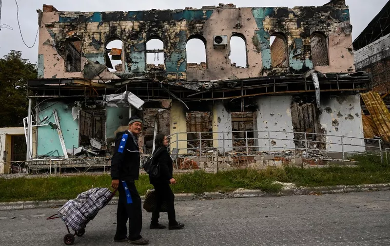 This photograph taken on September 11, 2022, shows a couple wheeling suitcases as they walk in front of a destroyed building in Izyum, Kharkiv Region, eastern Ukraine, amid the Russian invasion of Ukraine. - Ukraine forces said that their lightning counter-offensive took back more ground in the past 24 hours, as Russia replied with strikes on some of the recaptured ground. The territorial shifts were one of Russia's biggest reversals since its forces were turned back from Kyiv in the earliest days of the nearly seven months of fighting, yet Moscow signalled it was no closer to agreeing a negotiated peace. (Photo by Juan BARRETO / AFP)