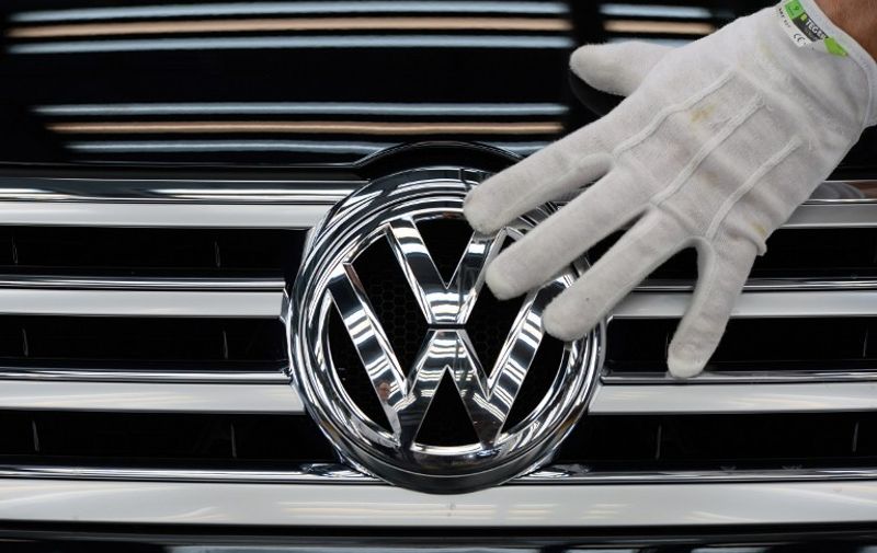 Picture taken on October 23, 2015 shows an employee of German car maker Volkswagen (VW) touching the VW logo on a Phaeton car at the company's Glaeserne Manufaktur (Transparent Factory) in Dresden, eastern Germany. German auto giant Volkswagen said on October 28, 2015 that the global pollution-cheating scam it is currently embroiled in pushed it deeply into the red in the third quarter and would hurt earnings for the whole of 2015.    AFP PHOTO / DPA / RALF HIRSCHBERGER   +++   GERMANY OUT / AFP PHOTO / DPA / RALF HIRSCHBERGER