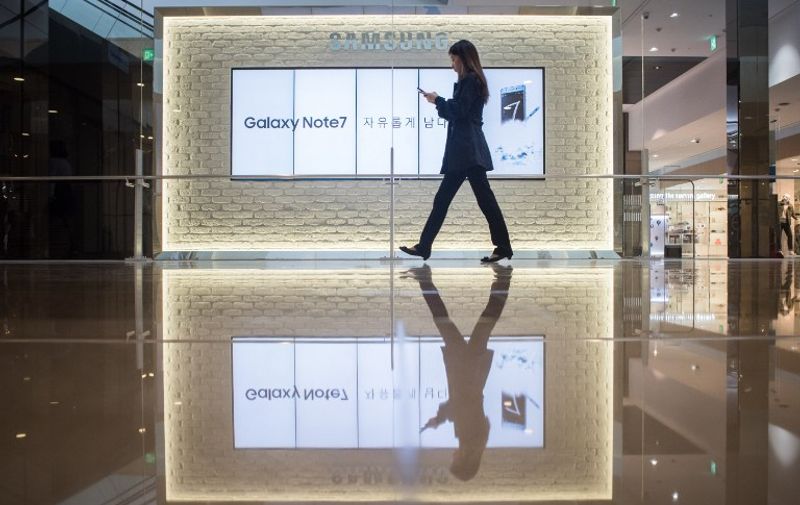 A woman looks at her mobile phone as she walks past advertisements for Samsung's Galaxy Note 7 device at a Samsung store in the Gangnam district of Seoul on October 11, 2016.
Samsung told customers worldwide to stop using their Galaxy Note 7 smartphones as it struggled to contain a snowballing safety crisis that threatens to derail the powerhouse global brand. / AFP PHOTO / Ed Jones