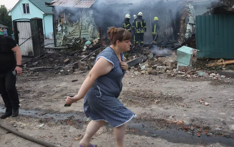 A woman walks past firefighters extinguishing a fire in a house that was damaged following a missile attack in a village outside Kyiv on August 30, 2023, amid the Russian invasion of Ukraine. (Photo by Anatolii STEPANOV / AFP)