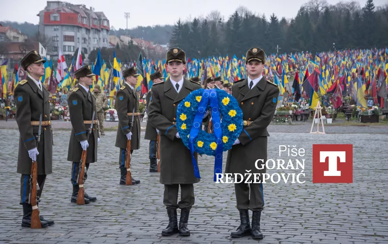 Počasna straža drži plavi vijенац s cvijećem ispred groblja s tisućama zastava u pozadini