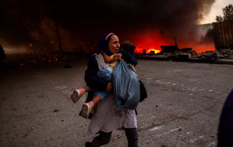 A migrant holds a girl as they flee a fire burning in the Moria camp on the island of Lesbos on September 9, 2020. - Thousands of asylum seekers on the Greek island of Lesbos fled for their lives on September 9, 2020 as a huge fire ripped through the camp of Moria, the country's largest and most notorious migrant facility. Over 12,000 men, women and children ran in panic out of containers and tents and into adjoining olive groves and fields as the fire destroyed most of the overcrowded, squalid camp. The blaze started just hours after the migration ministry said that 35 people had tested positive at the camp. (Photo by ANGELOS TZORTZINIS / AFP)
