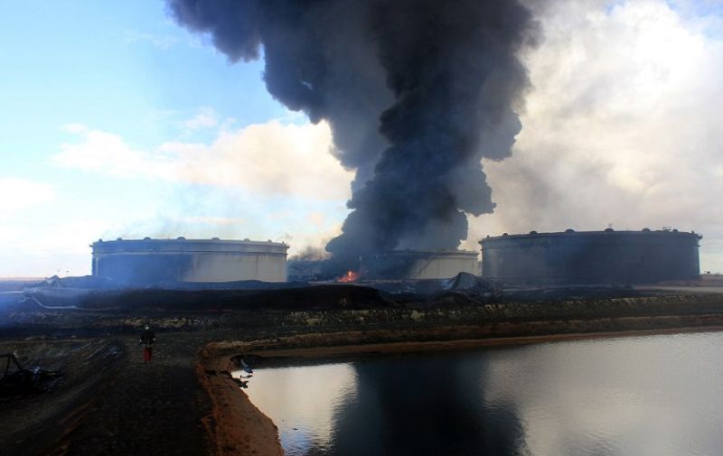 A Libyan oil worker walks infront of smoke rising from an oil facility in northern Libya's Ras Lanouf region on January 23, 2016, after it was set ablaze ealier in the week following fresh attacks launched by Islamic State (IS) group jihadists to seize key port terminals.
Firefighters battled the blaze at the oil facility for a third day, an official said, after an assault by jihadists aiming to seize export terminals.
 / AFP PHOTO / STRINGER