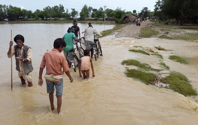In this photograph taken on August 16, 2014, Nepalese villagers walk through floodwaters in Banke District some 351kms (218 miles) west of Kathmandu. Rescuers in Nepal struggled to recover bodies and evacuate thousands after monsoon rains swept away houses, killing at least 85 people and sparking fears of a cholera outbreak, officials said.  AFP PHOTO/STR / AFP PHOTO / STRDEL