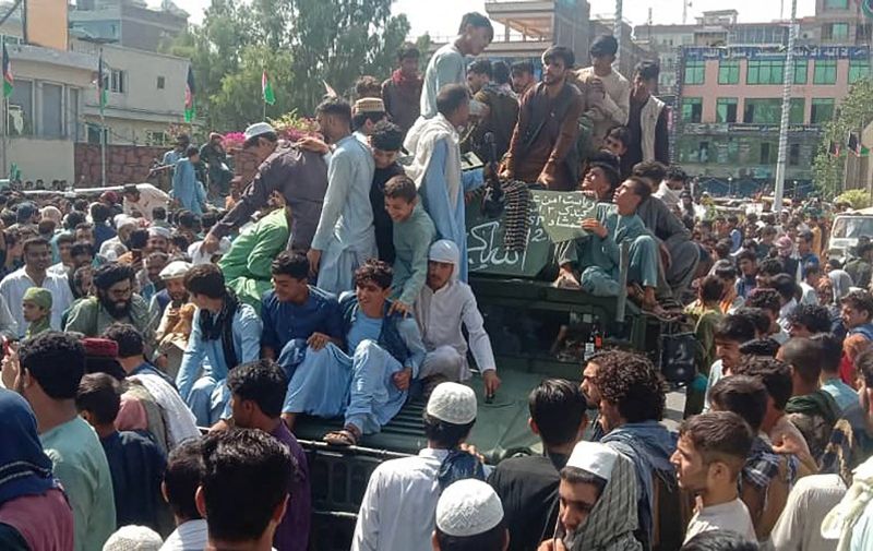 Taliban fighters and local people sit on an Afghan National Army (ANA) Humvee vehicle on a street in Jalalabad province on August 15, 2021. (Photo by - / AFP)