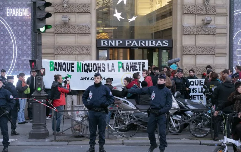 Police officers secure the area as activists stage a concert with French singer Kaddour Hadadi alias HK at the French Banking group BNP Paribas to protest against the company's polluting activity, in Paris on December 9, 2015.  / AFP / JACQUES DEMARTHON