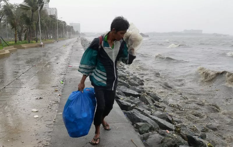 A man walks in the wind and rains brought on by typhoon Koppu along Roxas boulevard in Manila on October 18, 2015, as the typhoon hits Aurora province, northeast of Manila. Powerful Typhoon Koppu ripped off roofs, tore down trees and unleashed landslides and floods, forcing thousands to flee as it pummelled the northern Philippines on October 18, officials said.   AFP PHOTO / TED ALJIBE