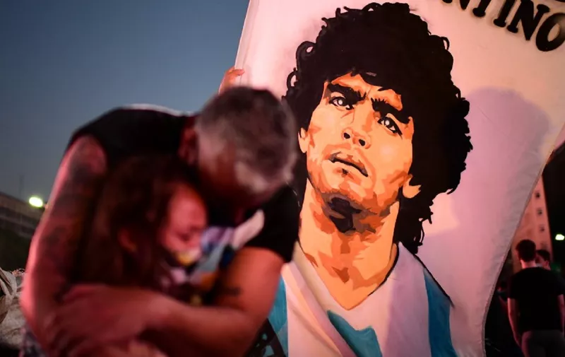 A father and her daughter, fans of Argentinian football legend Diego Maradona, mourn as they gather by the Obelisk to pay homage on the day of his death in Buenos Aires, on November 25, 2020. - The body of Argentine football legend Diego Maradona, who died earlier today, will lie in state at the presidential palace in Buenos Aires during three days of national mourning, the presidency announced. (Photo by RONALDO SCHEMIDT / AFP)
