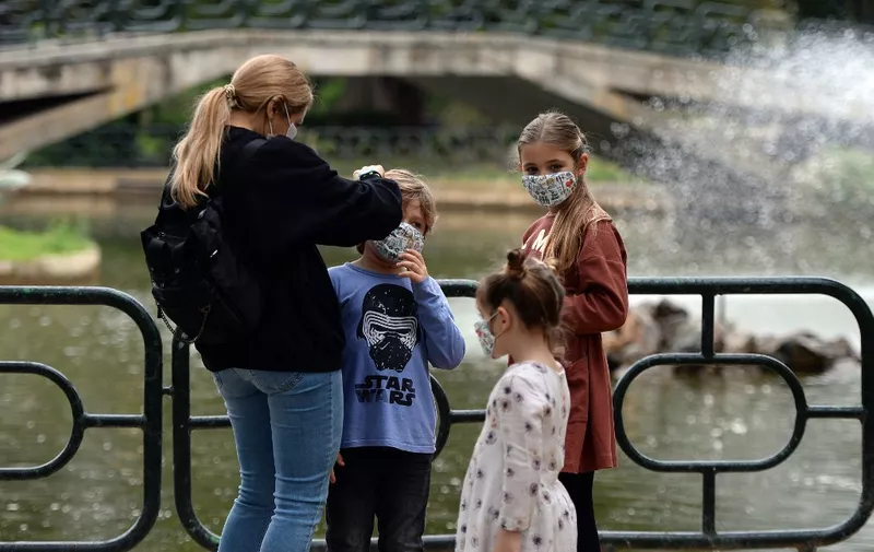 A woman adjusts her children's face masks in a park in Seville on April 26, 2020 amid a national lockdown to prevent the spread of the COVID-19 disease. - After six weeks stuck at home, Spain's children were being allowed out today to run, play or go for a walk as the government eased one of the world's toughest coronavirus lockdowns. Spain is one of the hardest hit countries, with a death toll running a more than 23,000 to put it behind only the United States and Italy despite stringent restrictions imposed from March 14, including keeping all children indoors. Today, with their scooters, tricycles or in prams, the children accompanied by their parents came out onto largely deserted streets. (Photo by CRISTINA QUICLER / AFP)